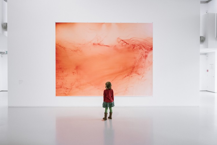 Ein Kind steht vor einer großen Fotoarbeit von Wolfgang Tillmans. Die gesamte Arbeit besteht aus roten Farbschlieren, die mal luftig, mal dicht das Papier bedecken.